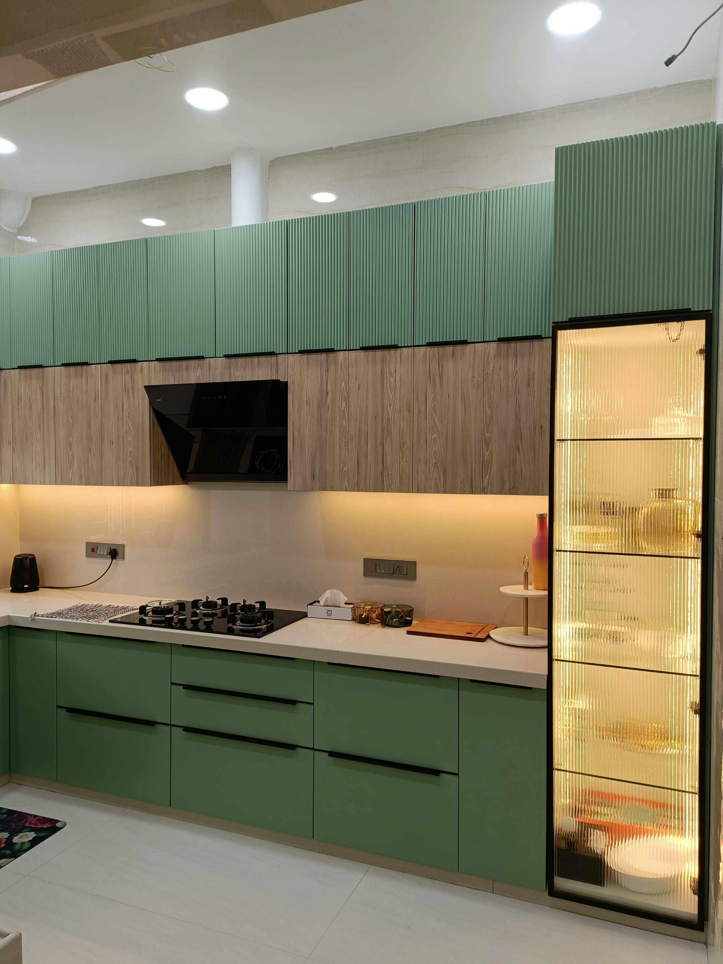 A green kitchen with a tall unit fronted in glass