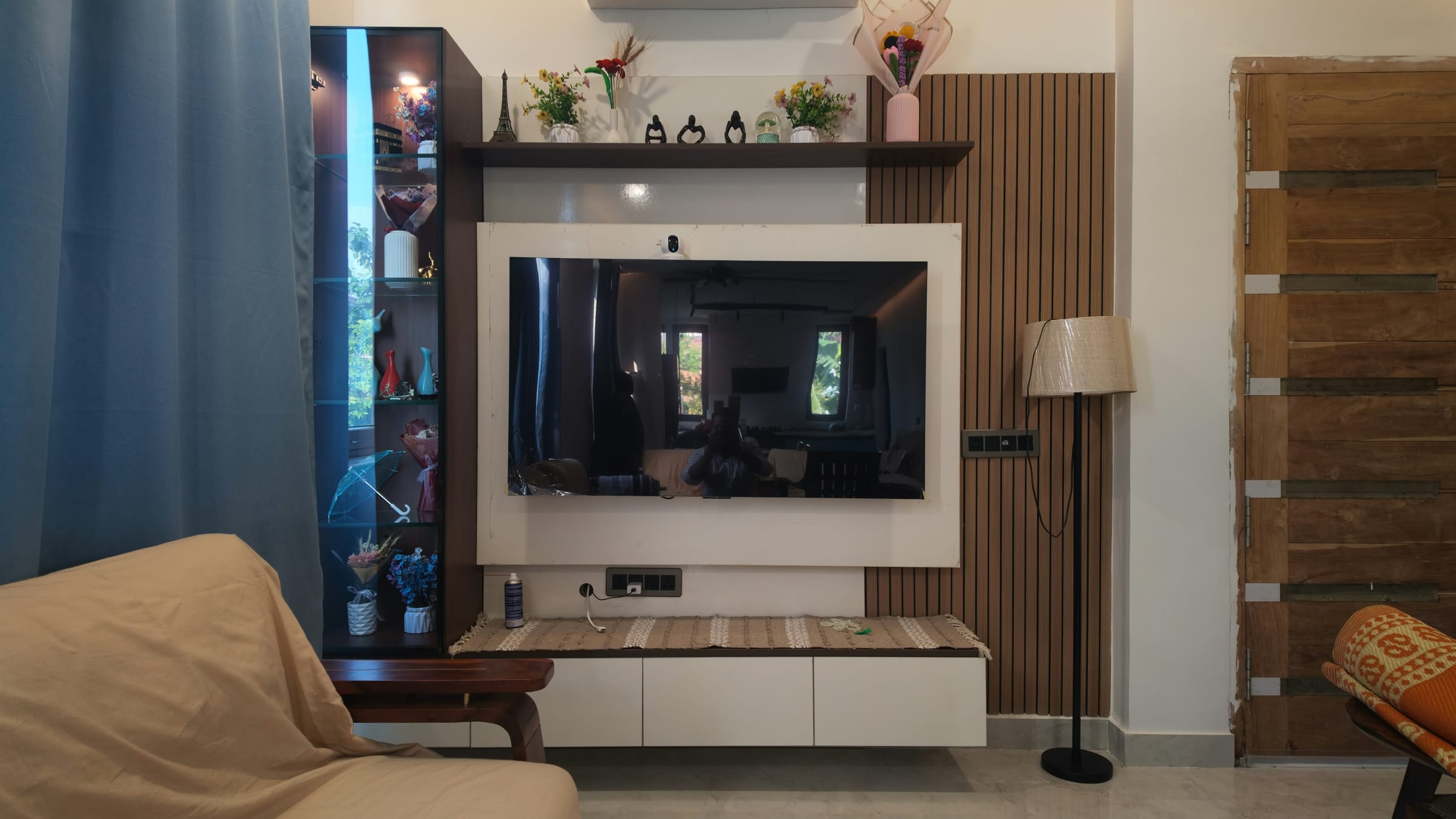 A television wall with a fluted wood panel to one side and a glass-fronted display column to the other